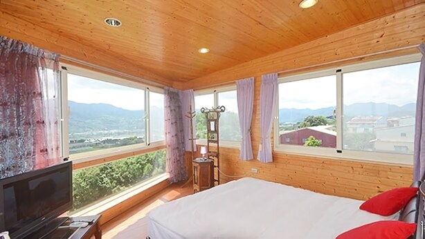 A bedroom with a bed, a TV, and large windows offering a mountain view. - Warm House Hostel (Taichung)