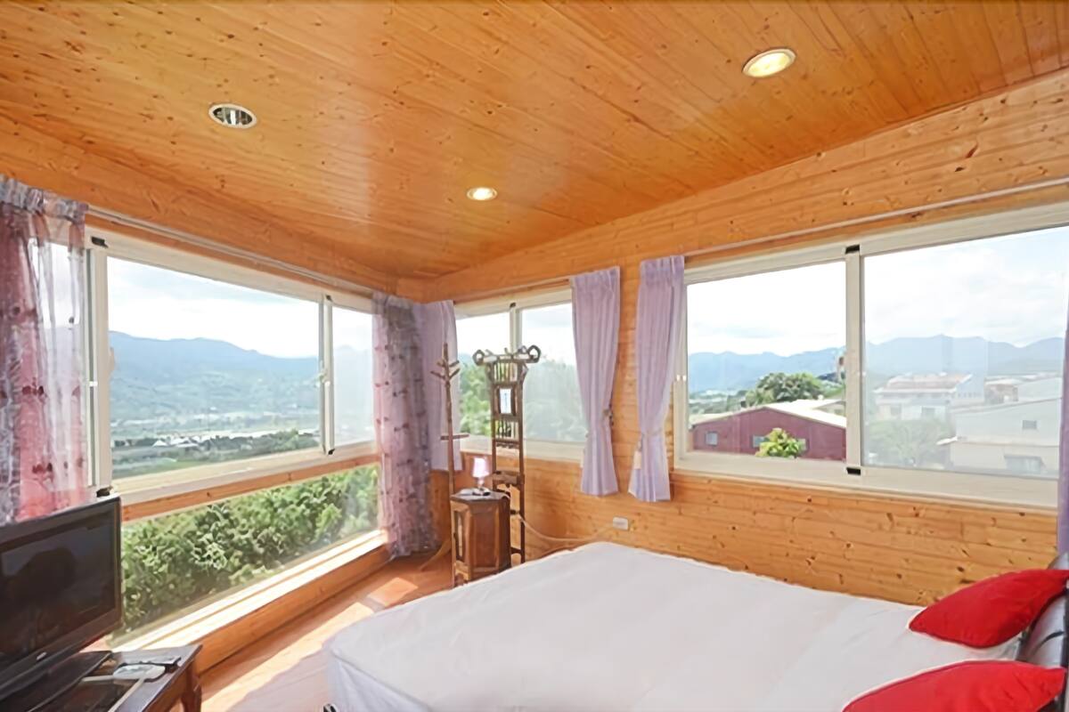 A bedroom with a bed, a TV, and large windows offering a mountain view.