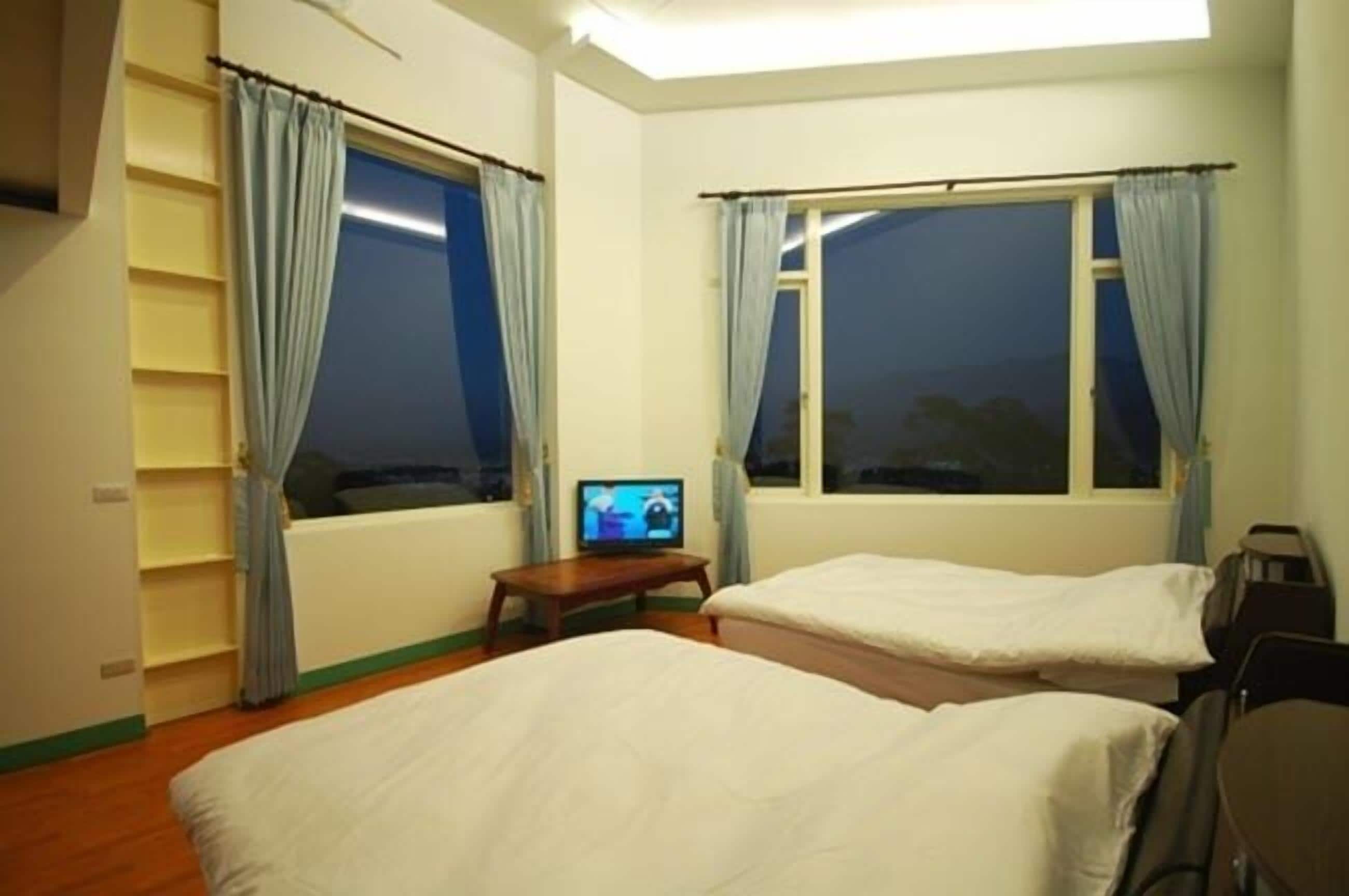 Una habitació d'hotel amb dos llits, televisió i finestres amb cortines.