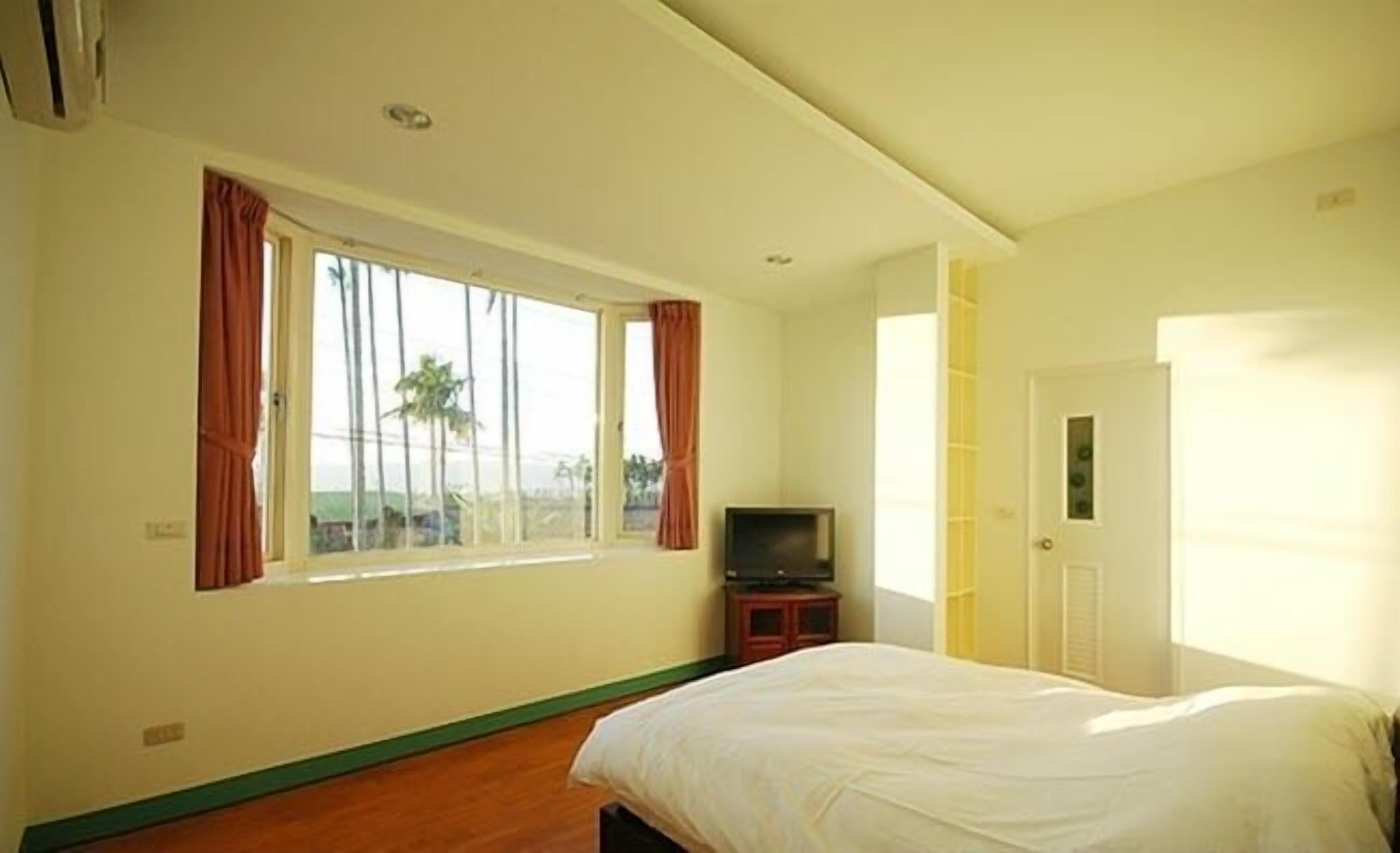 Un dormitorio con cama, televisor y ventana con cortinas.