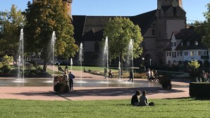 Un bâtiment historique doté de deux tours, d’une fontaine centrale et d’une cour pavée où se promènent des gens.