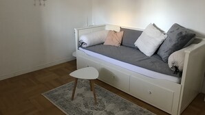 A white sofa with grey and white cushions, a small white side table, and a patterned rug on a wooden floor. - Small home in the spa area Freudenstadt (Freudenstadt)