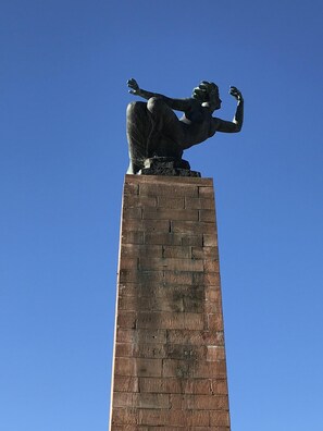 A statue on a brick pedestal against a clear blue sky.