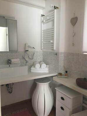 A modern bathroom with a white vanity, a mirror, a towel rack, and a heart-shaped decoration.