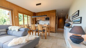 Eine moderne Küche mit Holzausstattung, ein Essbereich mit grauem Sofa und Sesseln sowie ein Blick ins Freie durch große Fenster.