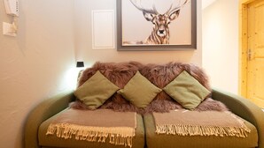 Ein Zimmer mit einem grünen Sofa, zwei grünen Kissen, einem Bilderrahmen mit einem Reh und einer Holztür.