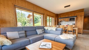 Ein modernes Wohnzimmer mit einer Eckcouch, Holzböden und großen Fenstern mit Blick ins Freie.