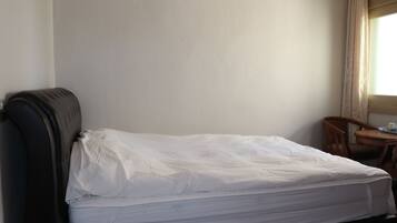 Una cama individual con cabecera, una mesita con una silla y una ventana con cortinas.