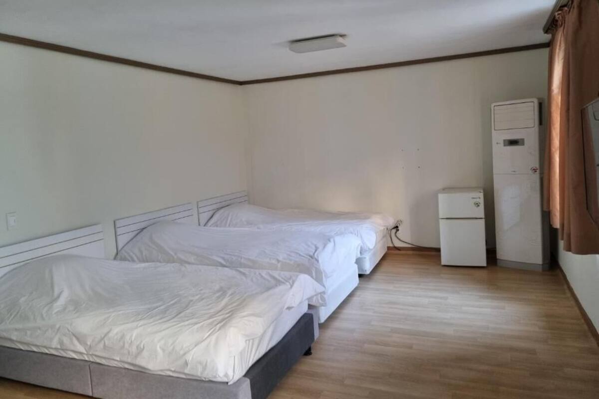 Un dormitorio con dos camas, un refrigerador blanco pequeño y suelo de madera.