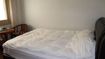 A single bed with white bedding in a room with a wooden chair and a small table.