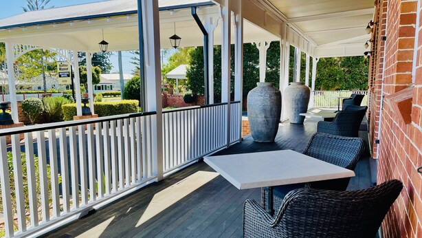 Een overdekt terras met een witte tafel, rieten stoelen, een bakstenen muur en grote vazen.