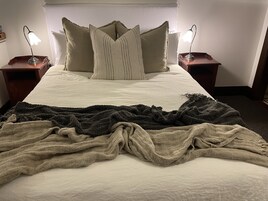 Una cama con sábana blanca, dos mesitas de noche con lámparas, y una colcha sobre la cama.