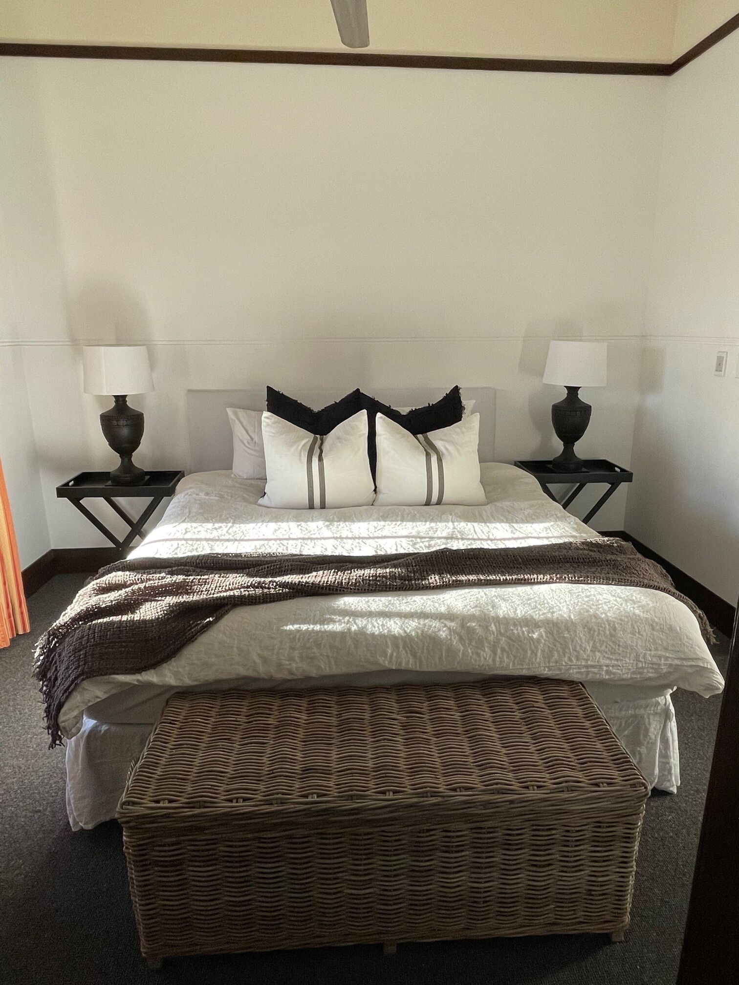 A neatly made bed with a striped blanket, two bedside tables with lamps, and a woven bench.