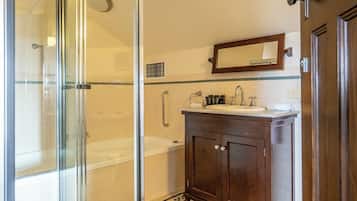 Un baño con cabina de ducha de vidrio, tocador de madera con espejo y suelo de baldosas con diseño geométrico.