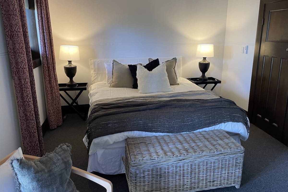 Ein ordentlich eingerichtetes Schlafzimmer mit einem Bett, zwei Nachttischen mit Lampen, einer Korbschaukel und einem Kleiderschrank.