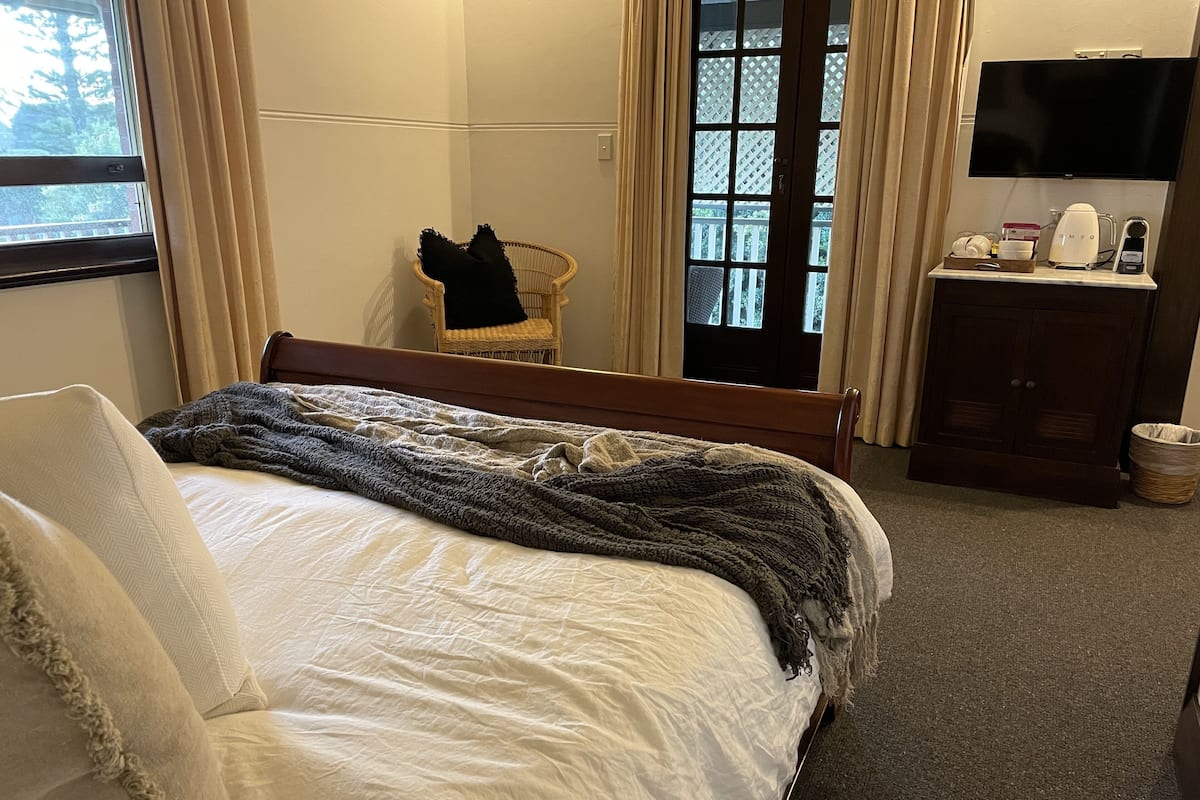Ein Hotelzimmer mit Bett, Sessel, Fernseher und kleinem Tisch mit Wasserkocher und weiteren Gegenständen.