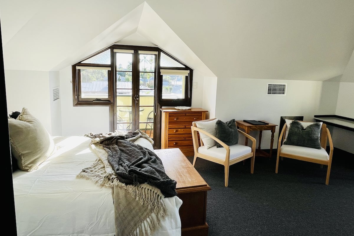 Ein Schlafzimmer mit schrägen Wänden, einem Bett, einer Holzkommode, zwei Stühlen und einem kleinen Tisch.