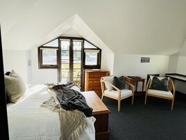 Un dormitorio con techo inclinado, una cama, un aparador de madera, dos sillas y una mesita.