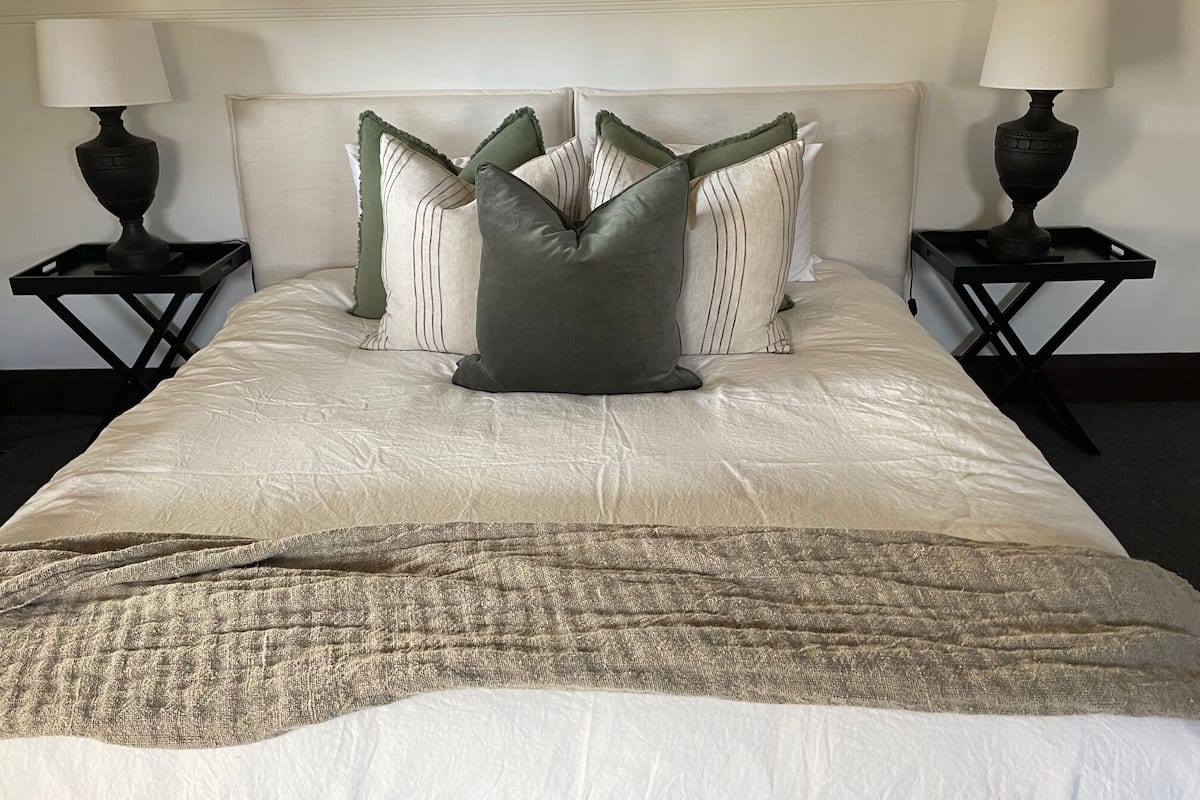 Ein ordentlich bezogenes Bett mit einer beigen Tagesdecke und einer gewebten Zudecke.