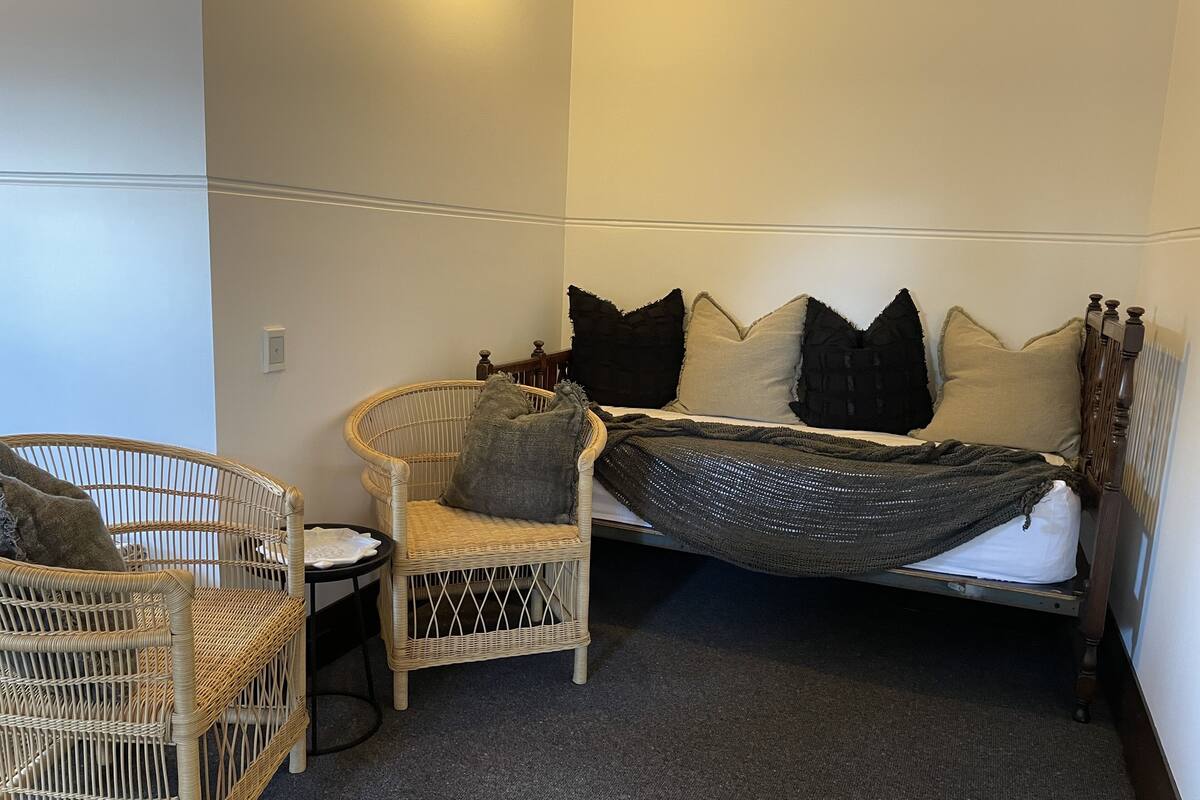 Ein Schlafzimmer mit einem Bett, zwei Korbstühlen, einem kleinen Tisch und einem Wandheizkörper.