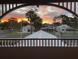 Vista desde la barandilla de un balcón a una calle residencial al atardecer, con casas y una montaña al fondo.