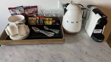 A breakfast tray with coffee maker, cups, and condiments on a marble countertop.