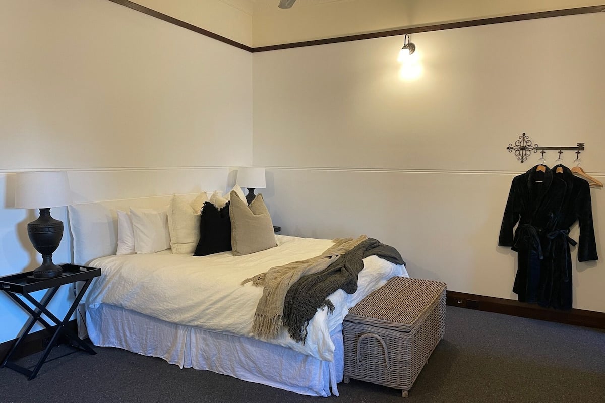 Ein ordentlich eingerichtetes Schlafzimmer mit Bett, Nachttisch, Lampe und einer Garderobe.