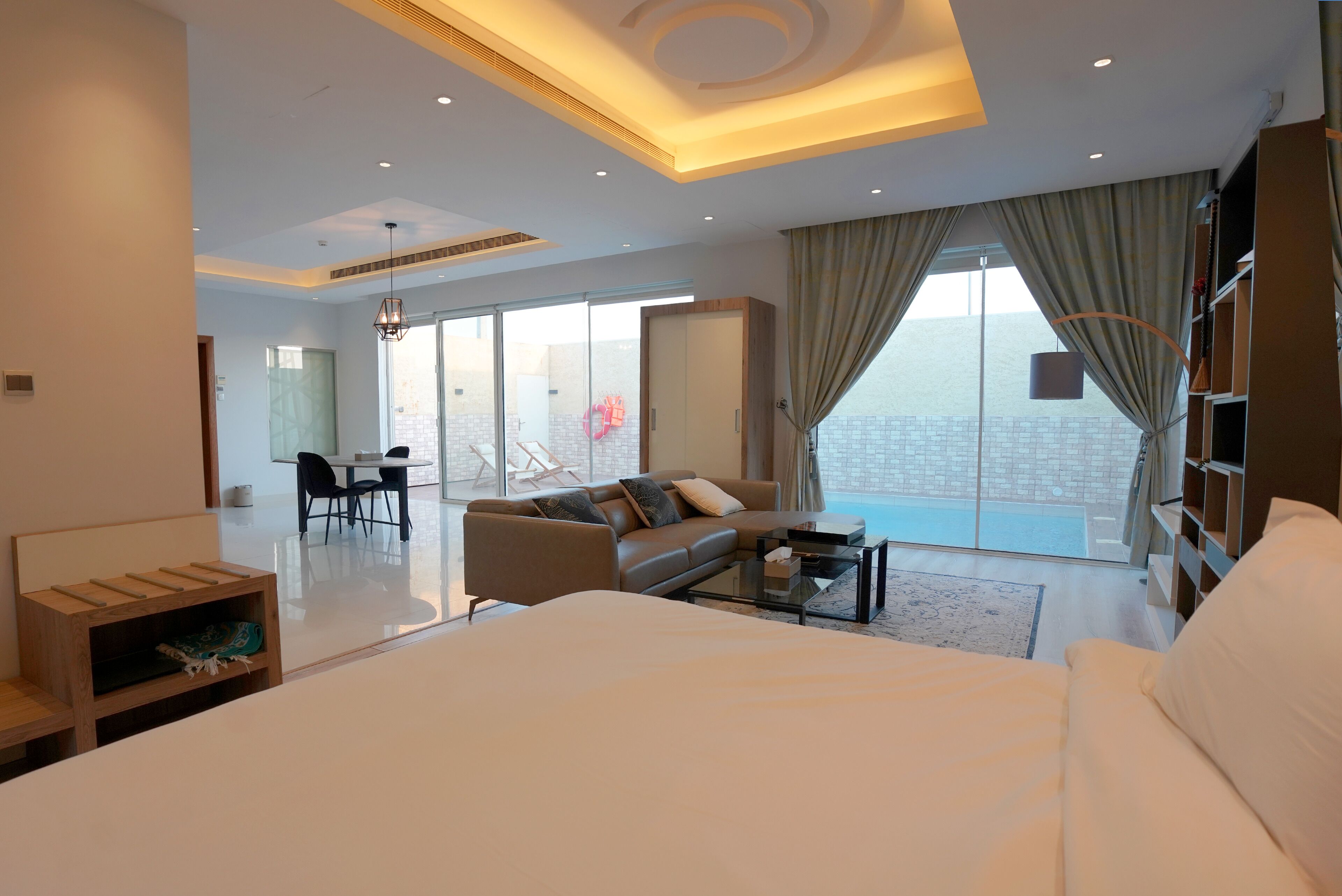 A modern hotel room with a large bed, a sofa, a coffee table, and a dining area with chairs.