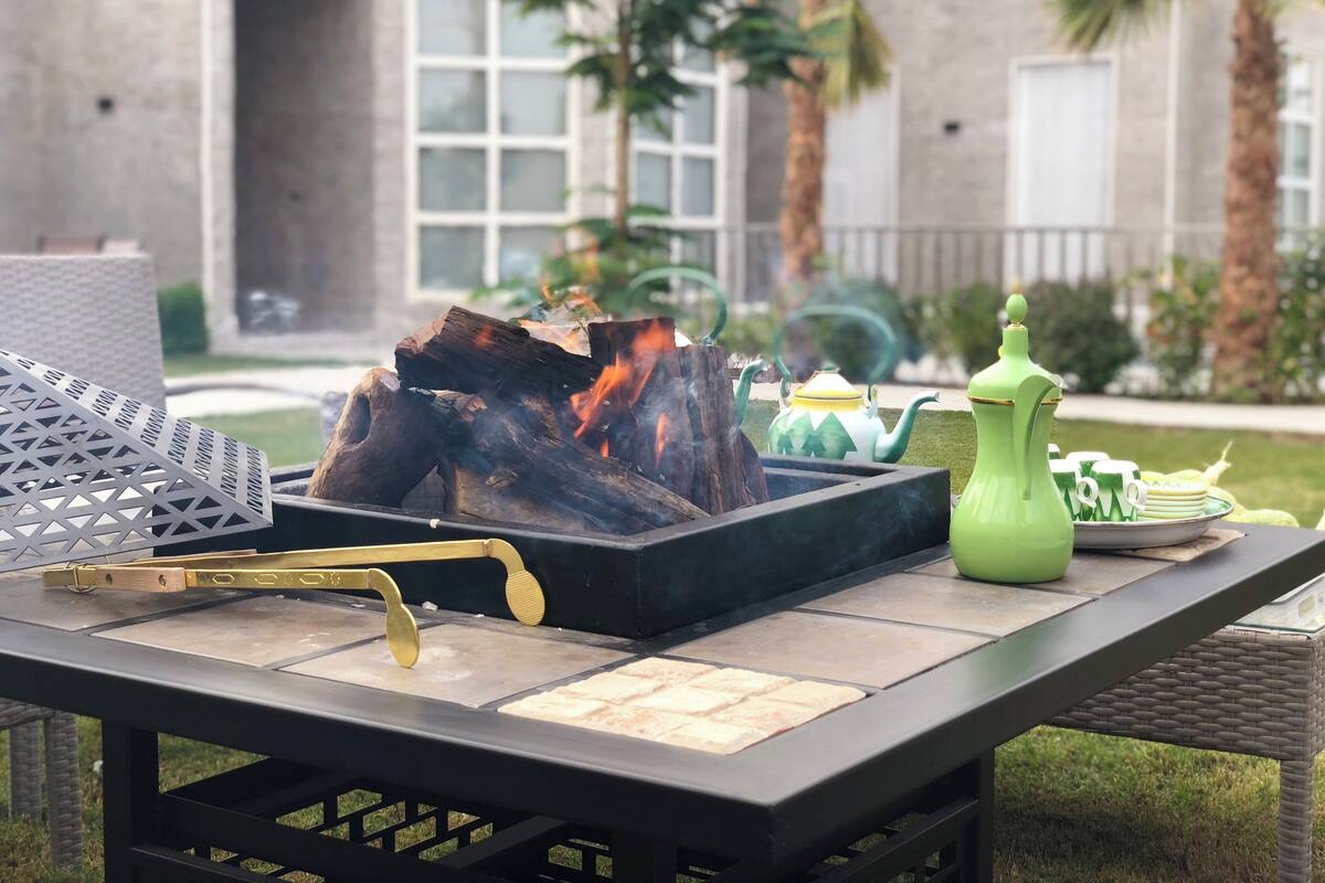 An outdoor seating area with a fire feature, a green teapot, and a tray with plates and cups.