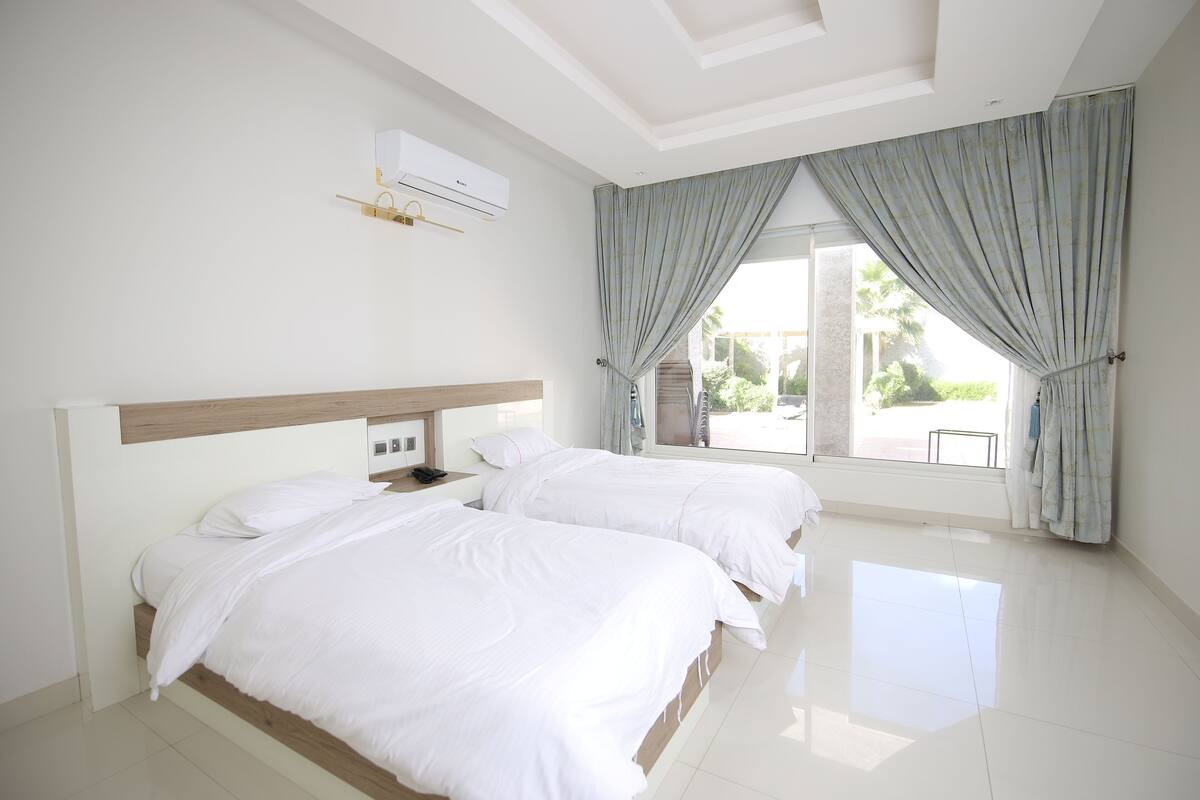 A hotel room with two beds, a window with curtains, a ceiling fan, and an air conditioning unit.