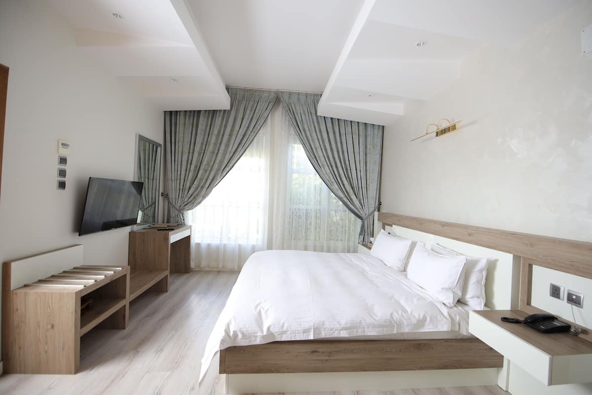 A modern hotel room with a large bed, a wooden bench, a TV, and a bedside table with a phone.