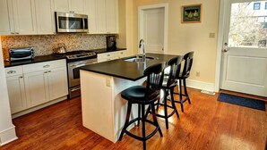 A kitchen with white cabinets, a microwave, a stove, a toaster, and a sink. There are three black barstools and a door with a glass panel. - Fully updated, 2 Blocks from the Beach, Sleeps 12 (Cape May)