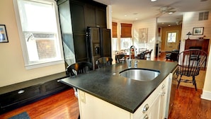 A modern kitchen with a central island, dark cabinetry, and a dining area with chairs and a table. - Fully updated, 2 Blocks from the Beach, Sleeps 12 (Cape May)