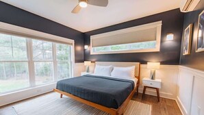 A bedroom with a bed, bedside tables, a ceiling fan, and large windows.