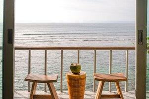 Un balcón con dos mesas de madera y un jarrón decorativo, con vista al océano.