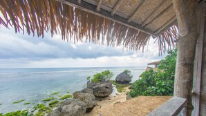 A beach view with a thatched roof structure, large rocks, and a sandy area with vegetation. - Le Cliff Bali (Pecatu)