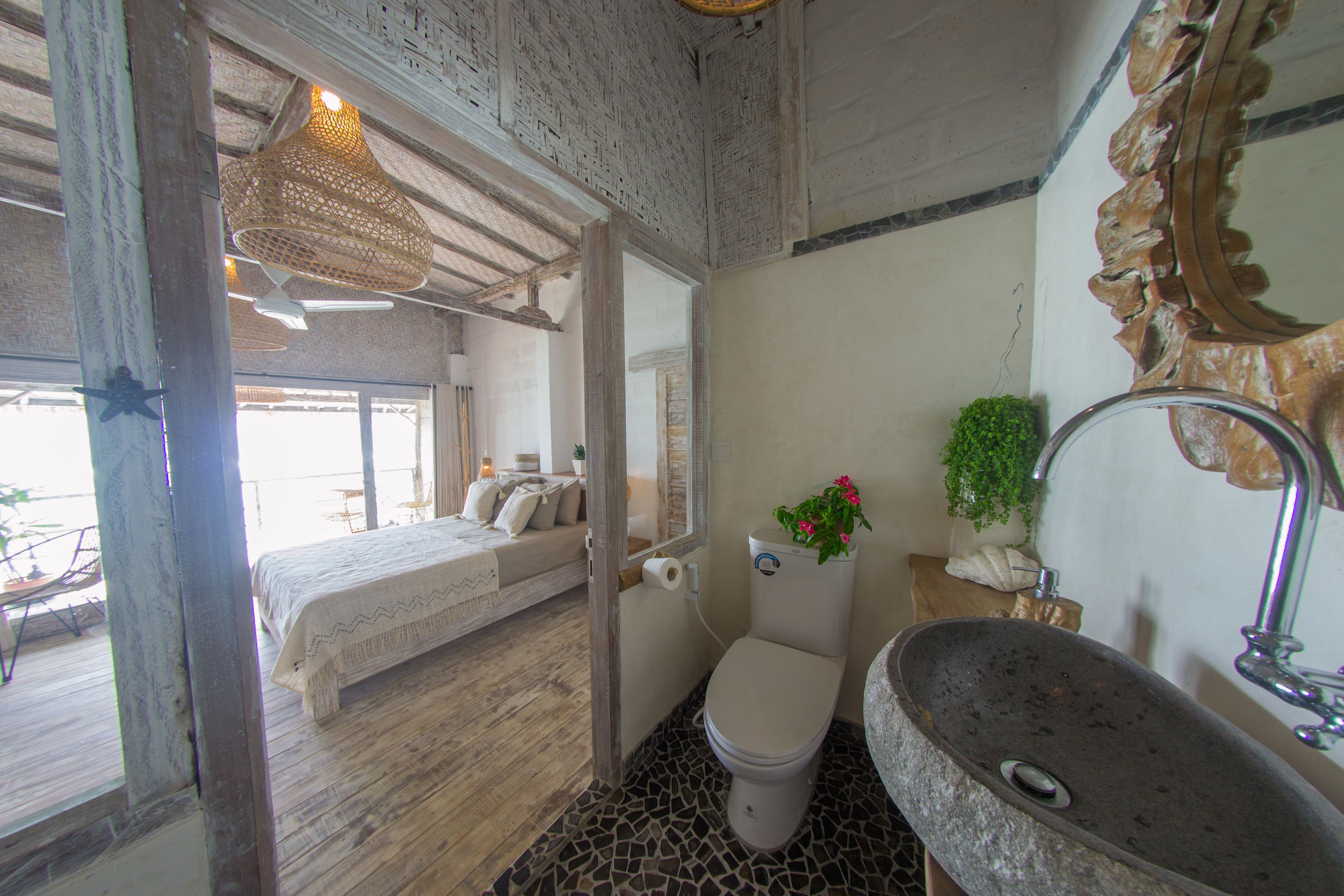 A bedroom with a bed, a bathroom with a sink and toilet, and a view of the outdoors.