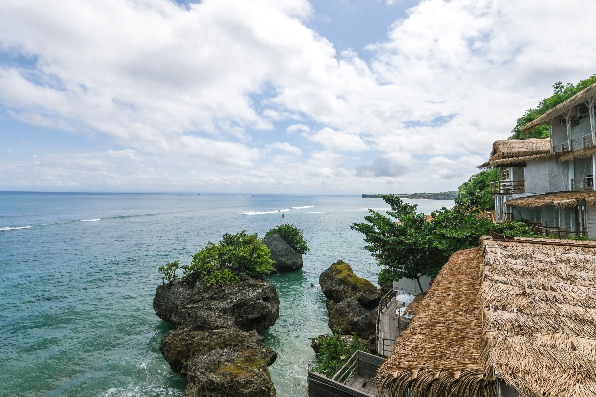 A coastal view with a thatched-roof building, clear blue sea, and rocky outcrops.
