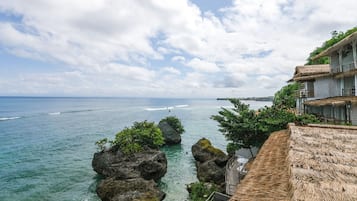 A coastal view with a thatched-roof building, clear blue sea, and rocky outcrops.
