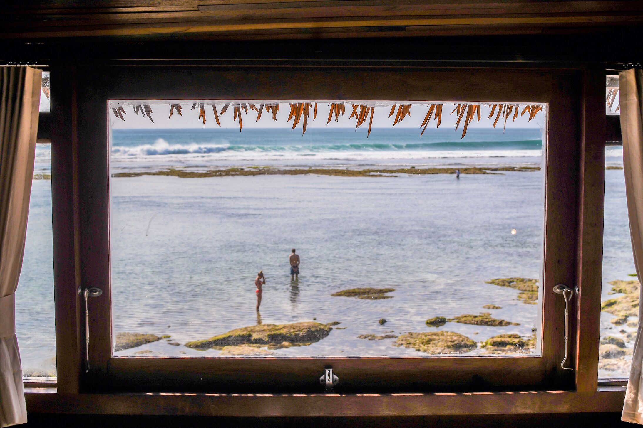 Une fenêtre donnant sur la plage, avec vue sur les personnes et les rochers.