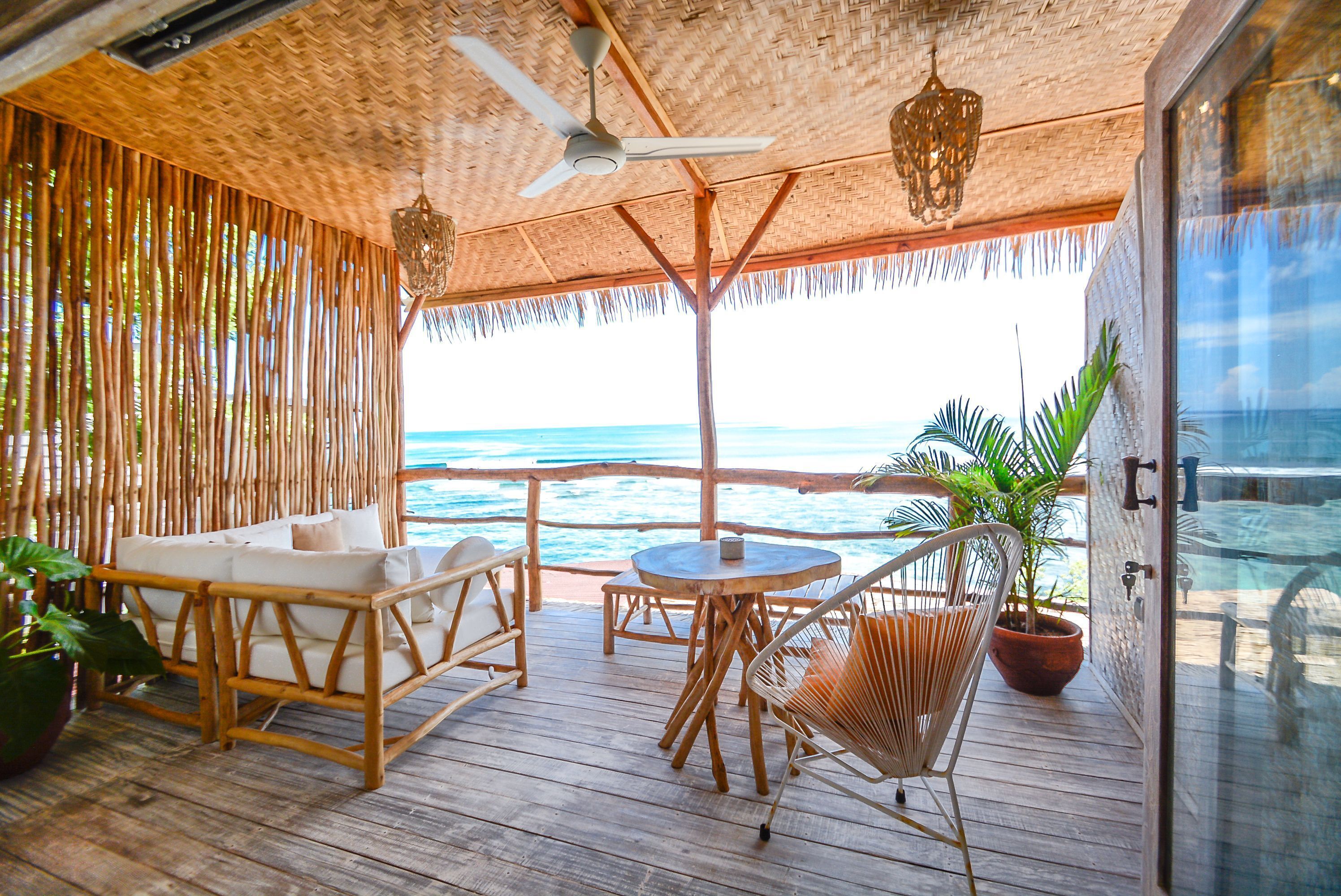 A wooden deck with wicker furniture, a ceiling fan, and a view of the ocean.