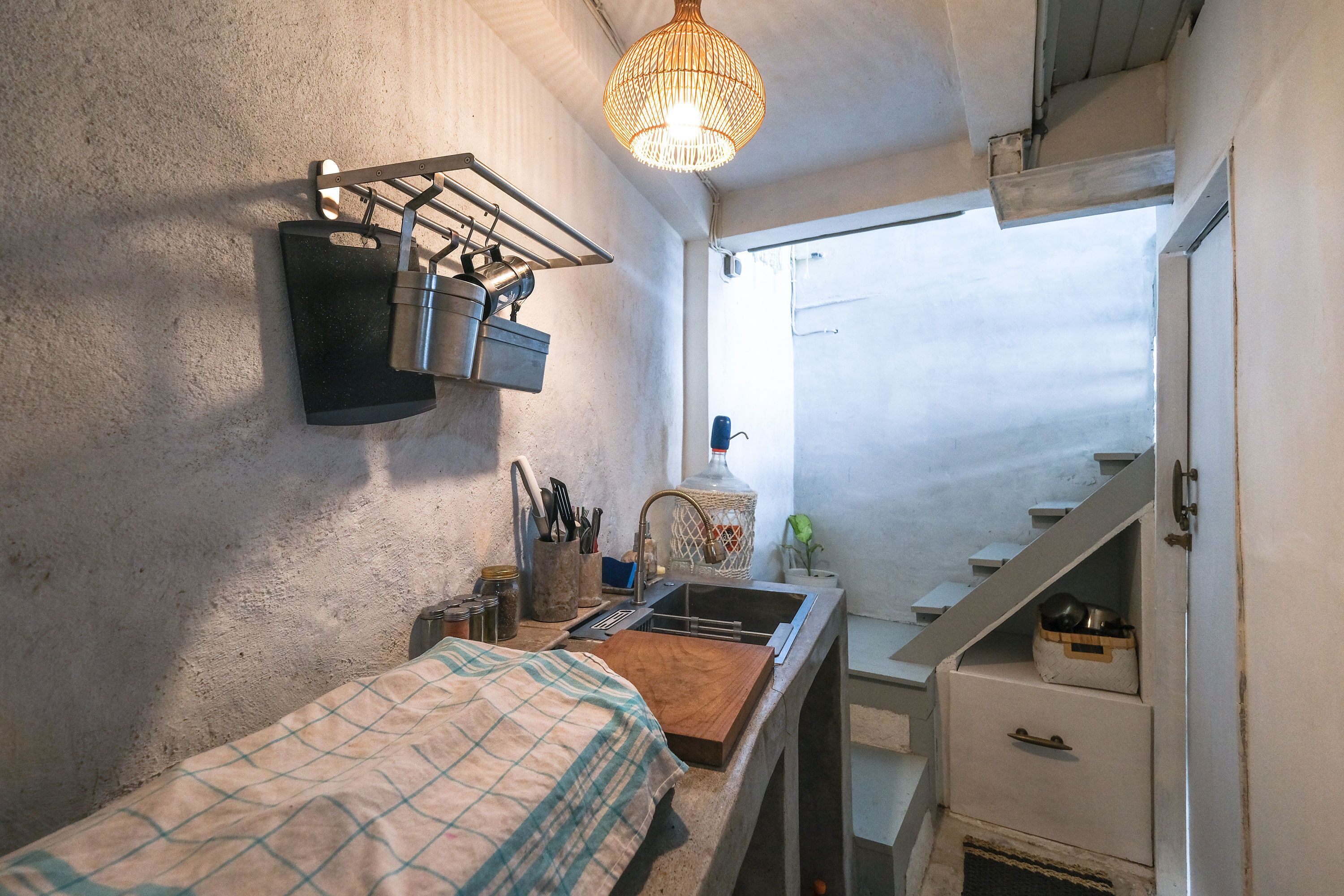 A compact kitchen with a sink, a hanging rack, and a wooden cutting board.