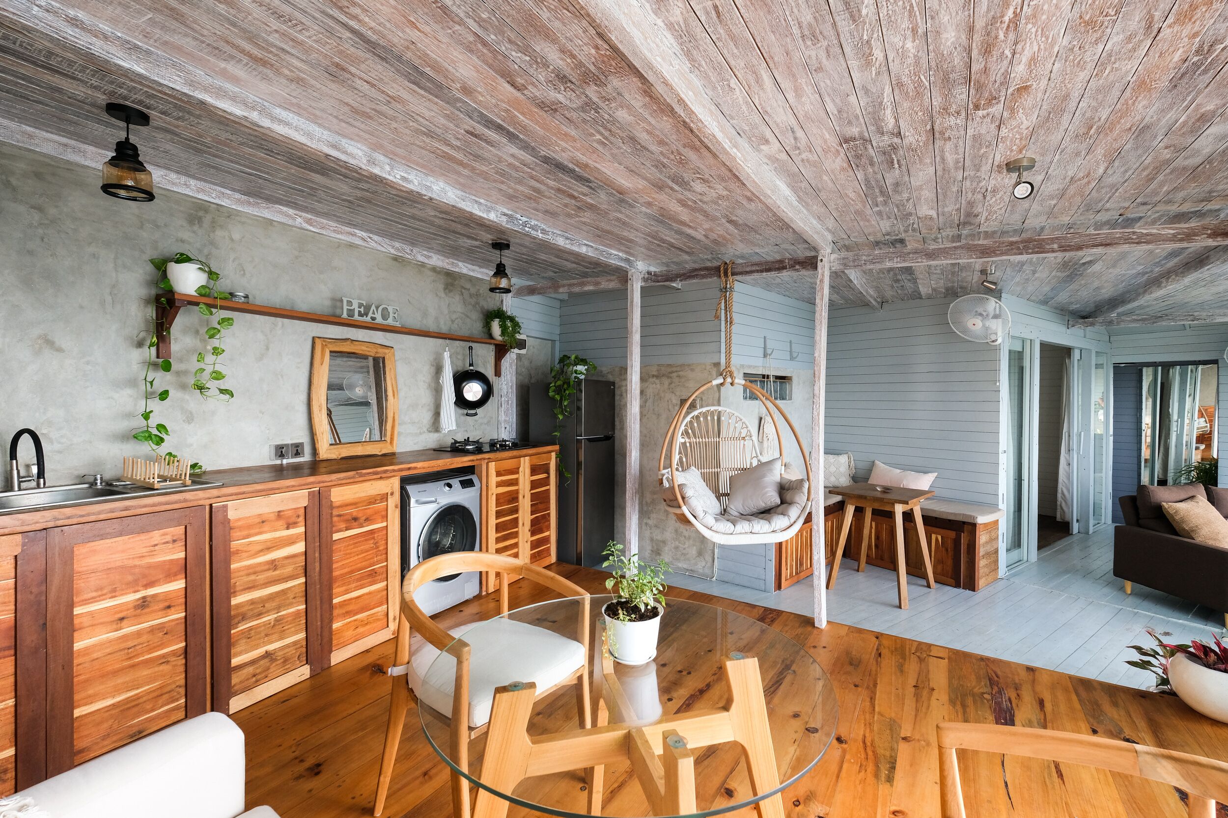 A rustic kitchen with wooden cabinets, a hanging chair, and a dining area with a glass table and chairs.