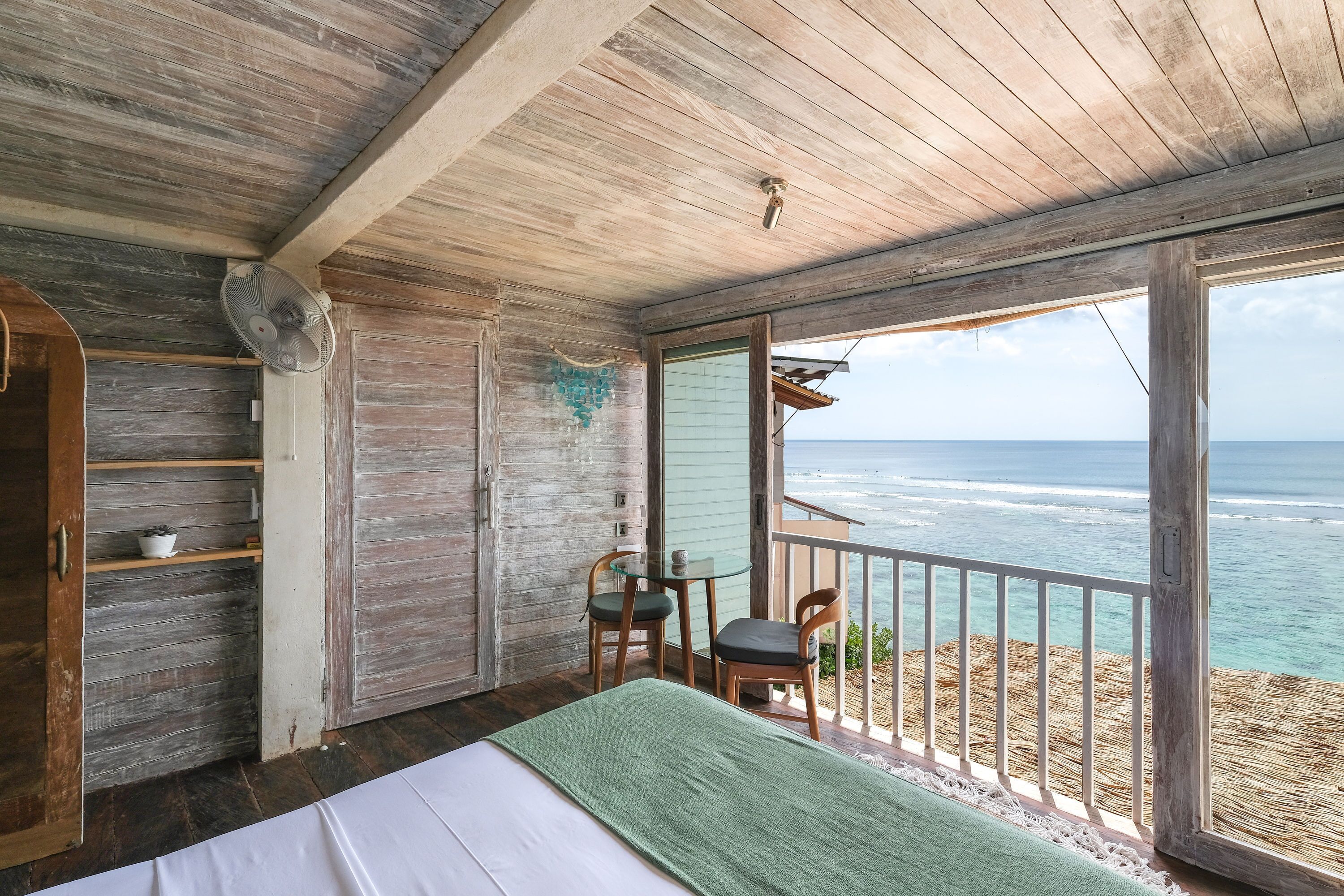 A bedroom with a bed, a table, two chairs, and a view of the ocean.