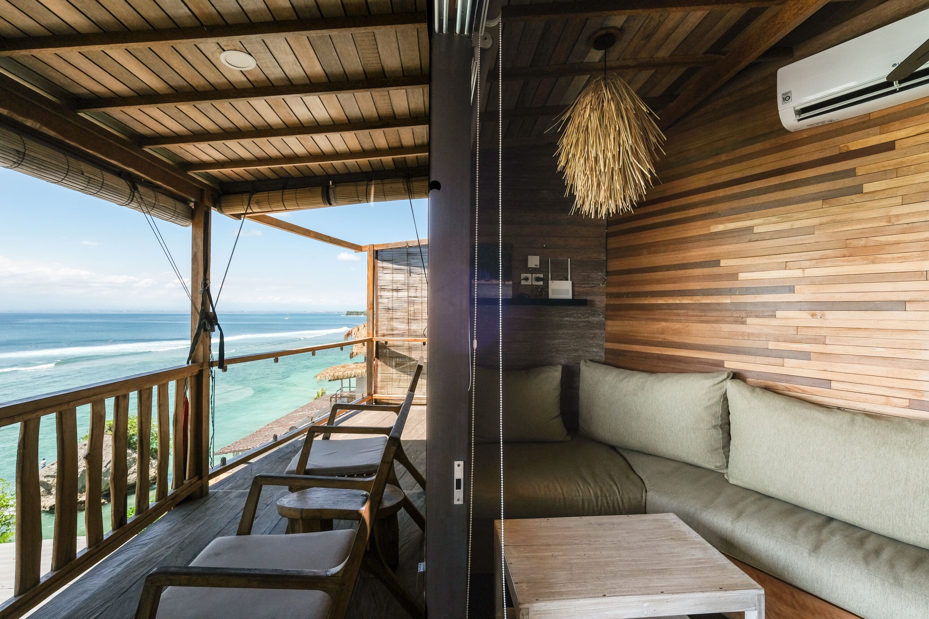 A wooden deck with a view of the ocean, a cushioned seating area, and a hanging light fixture.