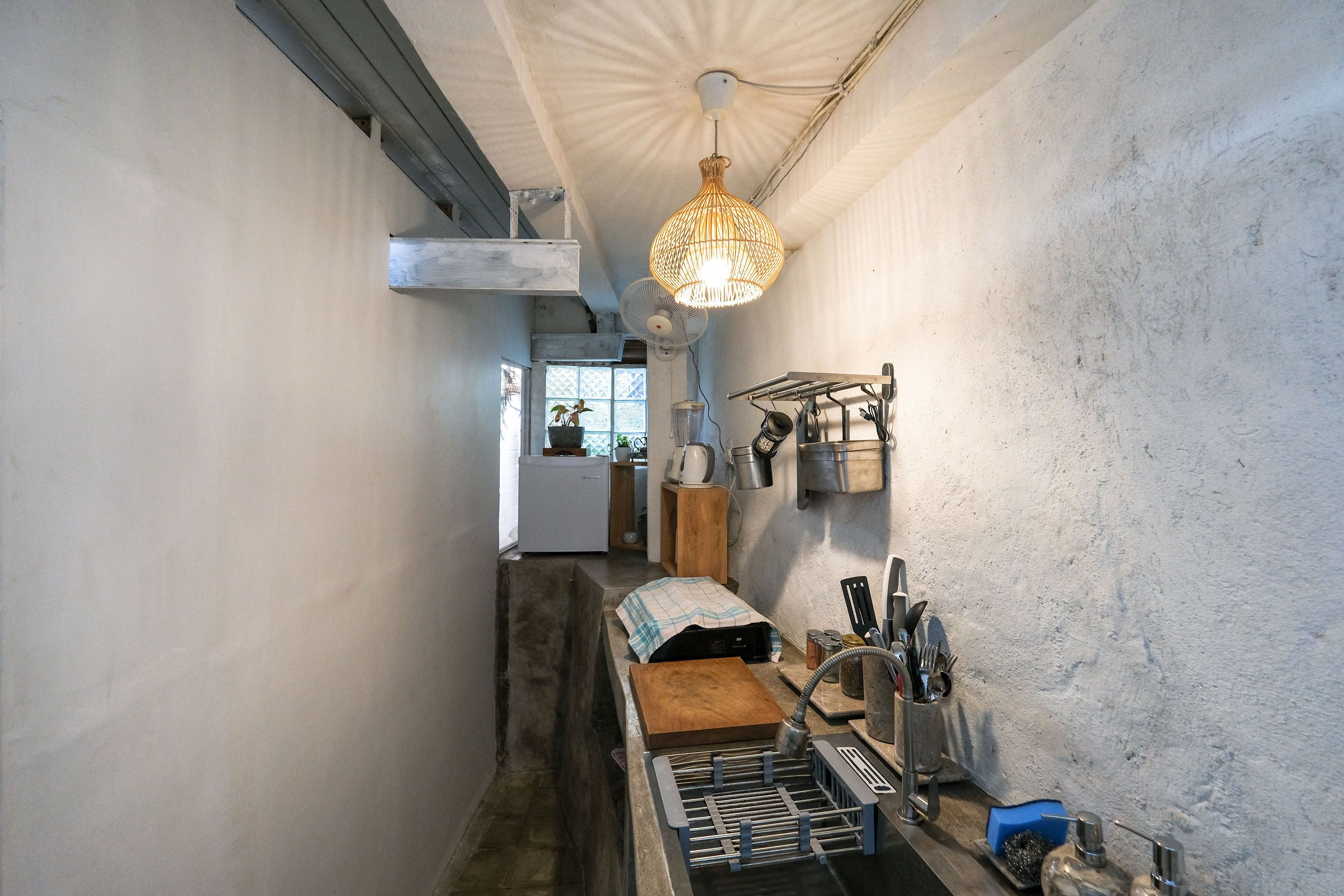 A narrow kitchen with a hanging light fixture, a built-in fan, and a sink with a drying rack.