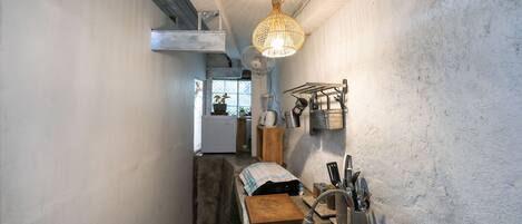 A narrow kitchen with a hanging light fixture, a built-in fan, and a sink with a drying rack.