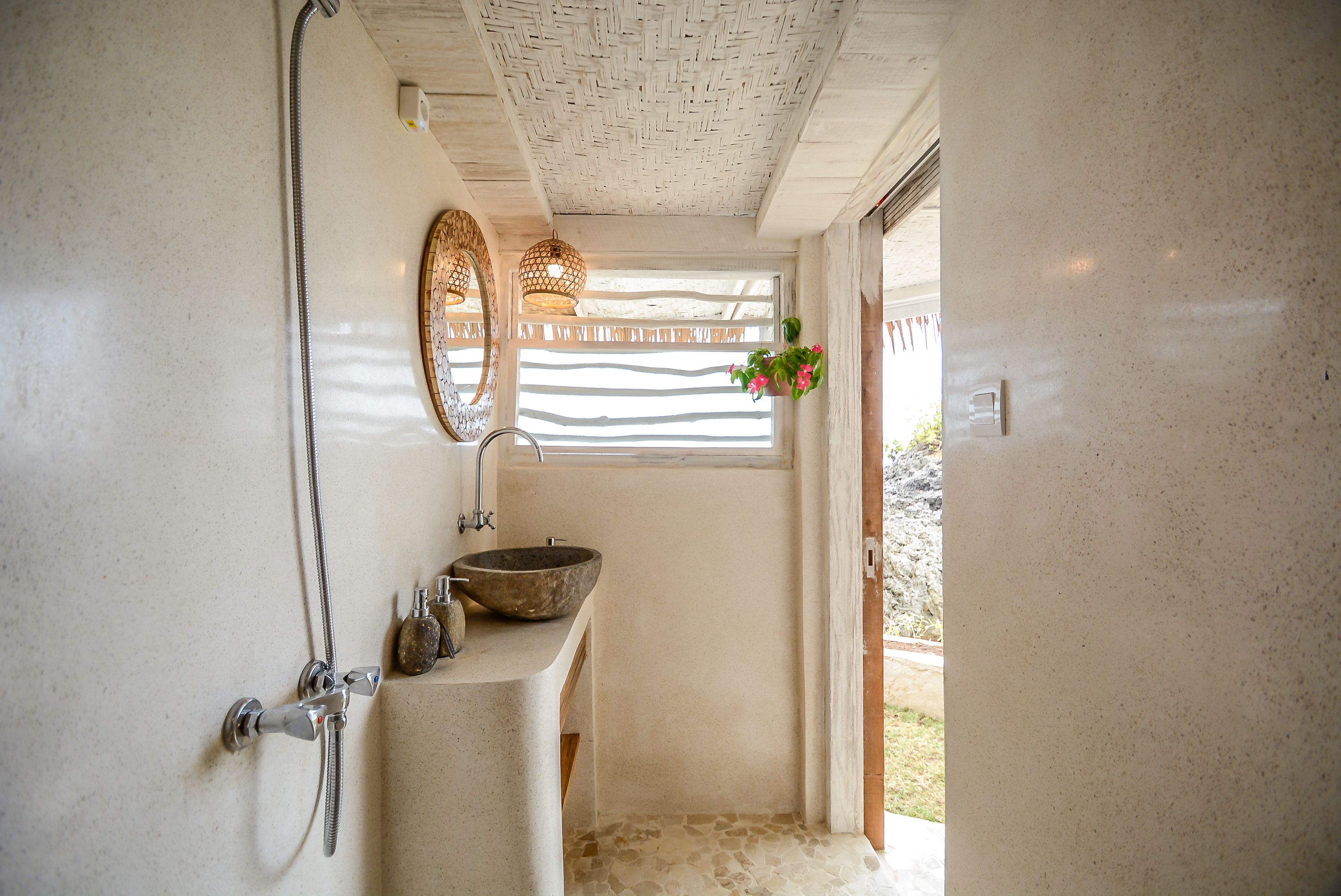 A bathroom with a large window, a stone sink, and a shower.