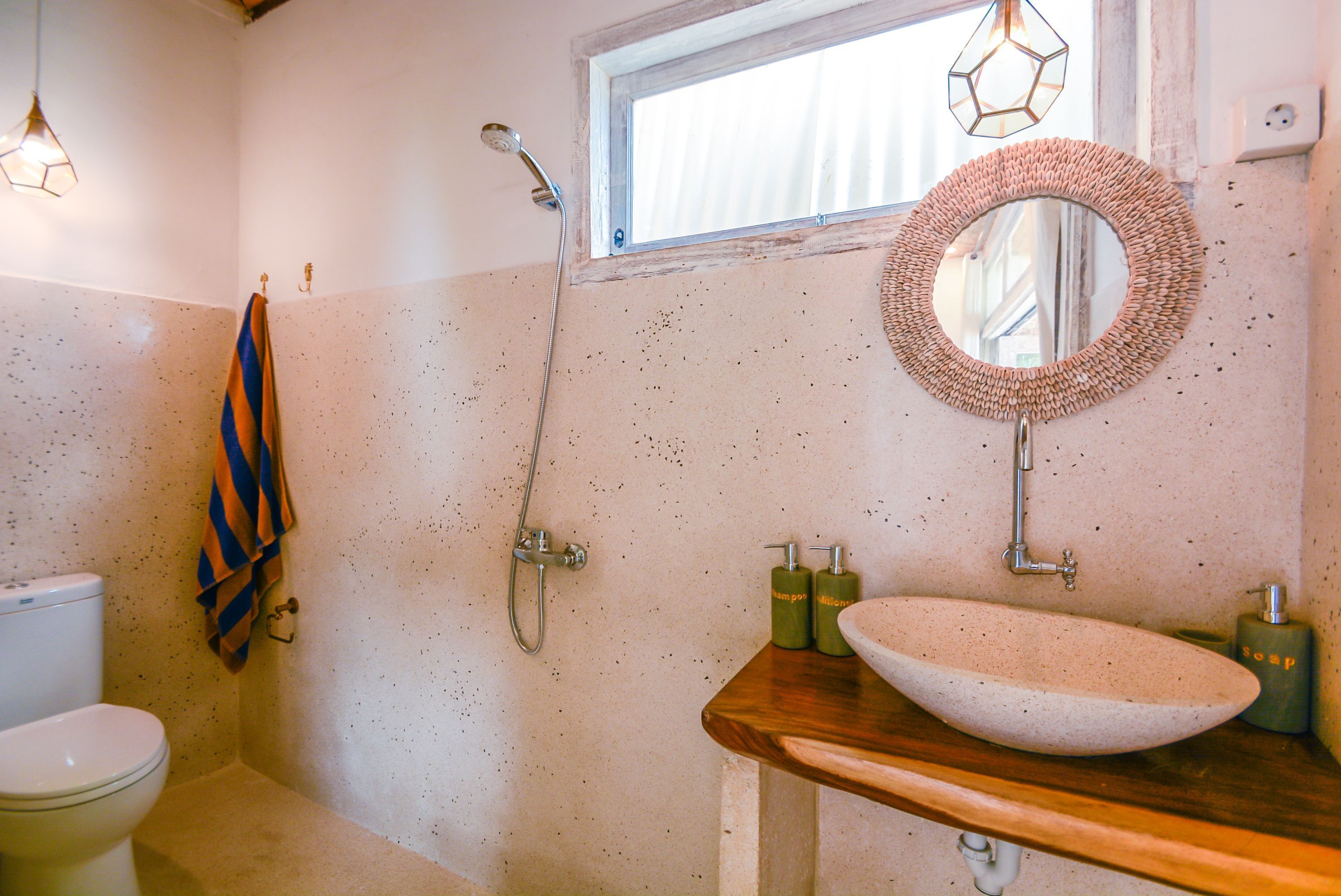Een badkamer met een wit toilet, een houten wastafelmeubel met een grote, ovale wasbak, een ronde spiegel en een douche met een handdouche.