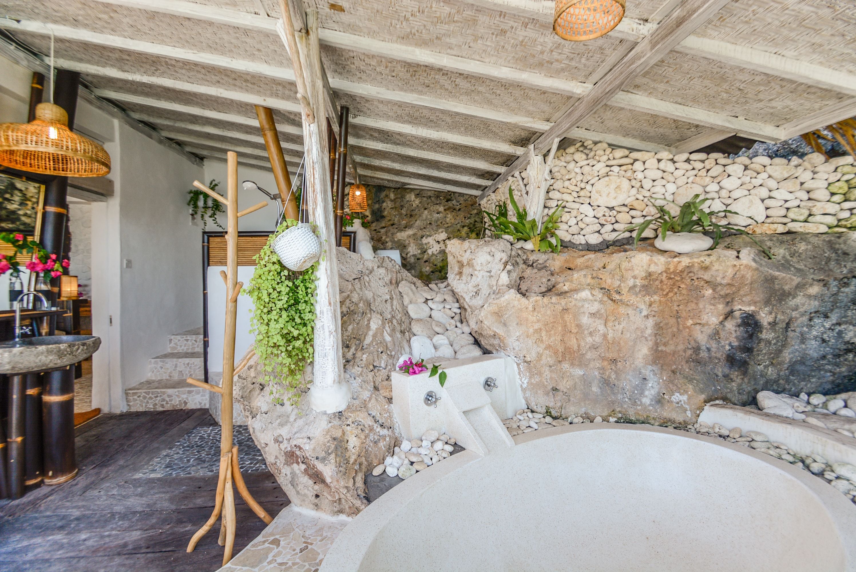 Una bañera de piedra con un fondo de pared de piedra, suelo de madera y una lámpara de mimbre colgante.
